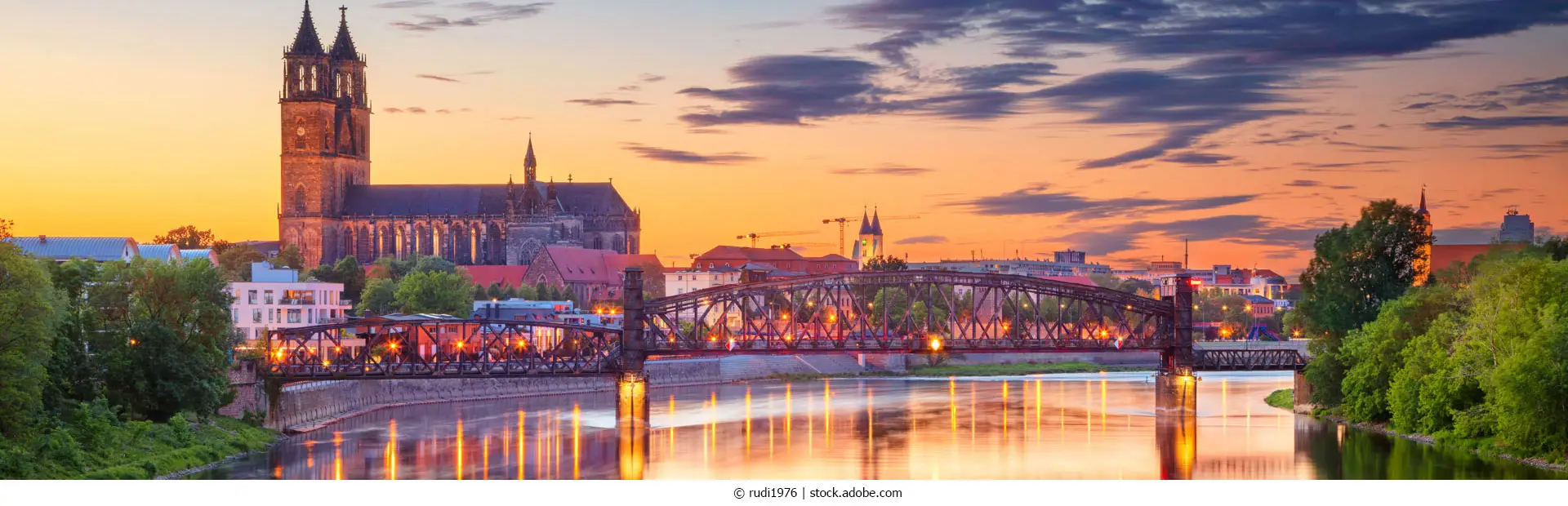 Stadtansicht von Magdeburg, Deutschland, mit der Spiegelung der Stadt in der Elbe bei Sonnenuntergang.